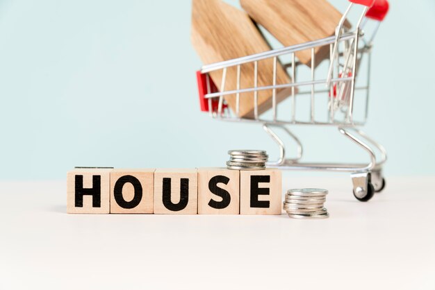 House wooden blocks with stack of coins in front of house model in the shopping cart