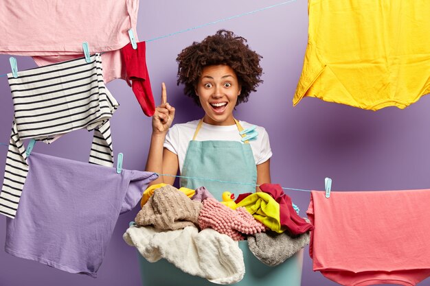 ハウスキーピングと洗濯のコンセプト。幸せな暗い肌の女性の家政婦はエプロンを着ています