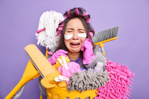 housewife applies hair rollers for making hairstyle wears patches under eyes undergoes beauty procedures while doing housework surrounded by cleaning tools does laundry