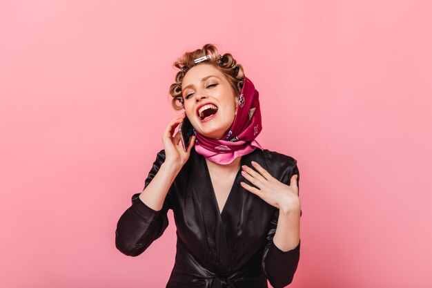 Housewife in black dressing gown laughs and talks on phone on pink wall