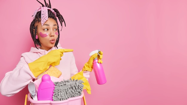 無料写真 主婦は、清掃サービスの準備ができているスプレー洗剤を持っています コピースペースに脇にあることを示します アイデアやヒントを与える ゴム手袋を着用します ピンクに隔離されたカジュアルな服を着ます