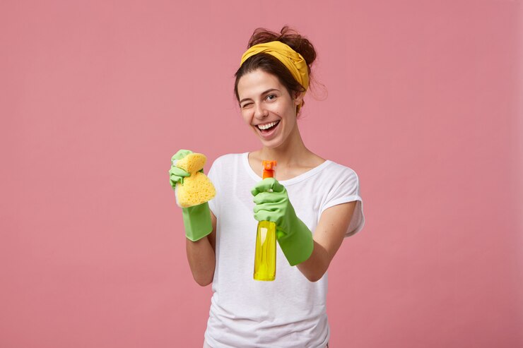 Free Photo housewife in white t-shirt and green gloves holding sponge and cleaner in hands blinking with her eyes having glad expression while washing. young pretty female doing domestic work