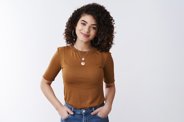 How can help you. Gentle lovely curly hair charming young woman hold hands jeans pockets confident friendly smile tilting head listen customer interesting story listen, white background