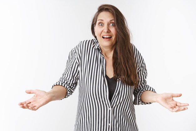 How did it happen Clueless and confused charming elderly lady in striped blouse with wrinkles shrugging with hands spread sideways surprised and unaware smiling uncertain over white background