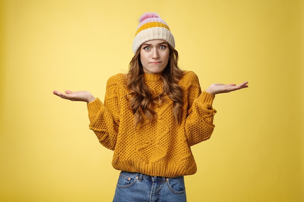 How should I know. Portrait confused perplexed worried cute female assistant shrugging spread hands sideways clueless unaware cannot understand what happened unsure, unaware yellow background