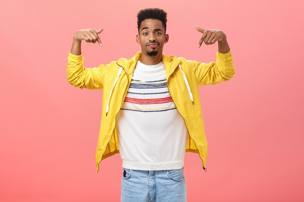 How you like my style. Cool and handsome stylish young man with beard in trendy yellow jacket over t-shirt raising hands pointing at himself smirking and raising eyebrow being unsure how he looks.