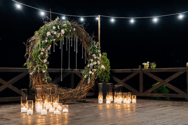 Huge decorative circle made of willow, greenery and pale orange roses with burning candles