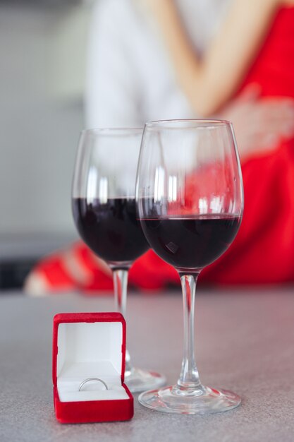 hugging beautiful couple. Glasses with wine and box with ring on table