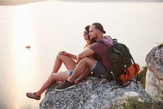 Hugging couple with backpack sitting on top of rock mountain