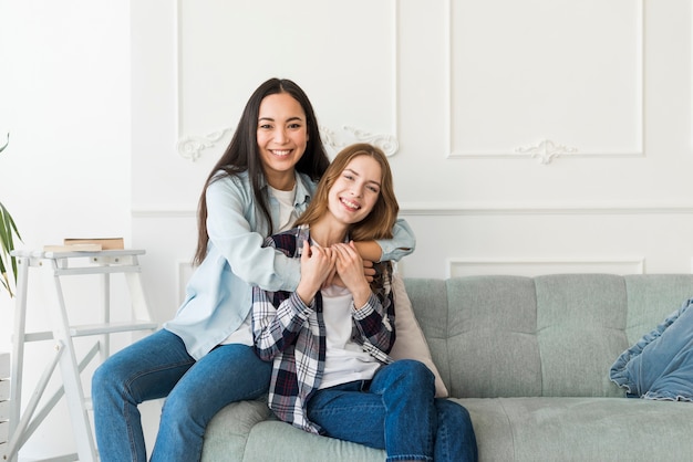 Hugging ladies sitting on couch and smiling