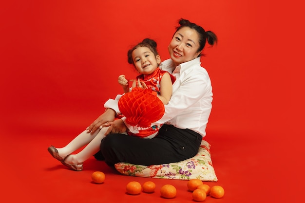 Abbracciare, sorridere felice, tenendo in mano le lanterne. . ritratto asiatico della figlia e della madre sulla parete rossa in vestiti tradizionali. celebrazione, emozioni umane, vacanze. copyspace.