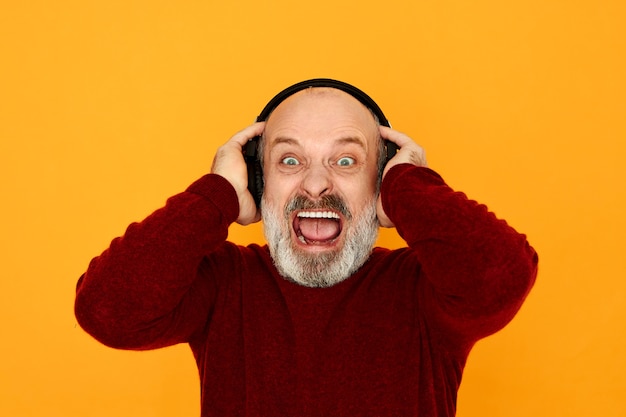 Human emotions, electronic devices and modern technology concept. emotional outraged elderly man listening to sports radio stream using earphones shouting