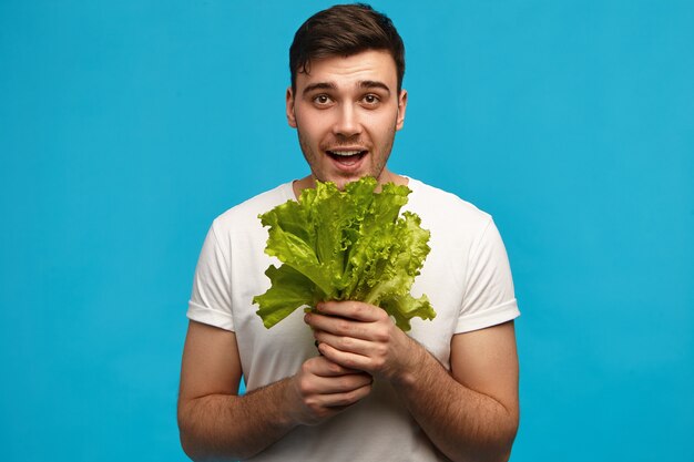 인간의 감정과 감정. 즐거운 젊은 백인 남자는 좋은 수확에 행복 신선한 야채 냄새를 흡입 파삭 파삭 한 녹색 양상추의 고립 된 지주 무리를 포즈. 음식과 영양 개념