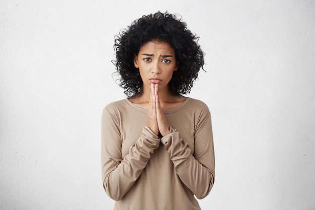 Free photo human emotions, feelings, reaction and attitude. beautiful student woman with afro hairstyle holding hands in prayer, begging professor to give her another chance on examination, having beseeching look