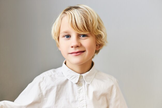 인간의 감정, 반응 및 감정. 금발 머리와 파란 눈을 가진 잘 생긴 귀여운 남학생의 초상화는 흰 셔츠에 격리 된 포즈,