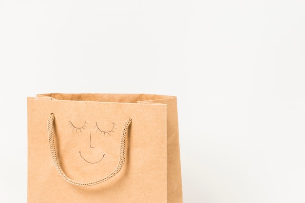 Human face drawn on brown paper bag against white surface