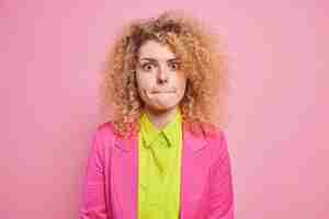 Free photo human face expressions. curly haired young woman with surprised expression presses lips feels worried