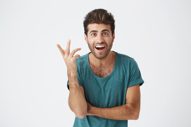 Human face expressions, emotions and feelings. Astonished and surprised bearded young man in blue t-shirt pointing at blank  wall, telling that he has an idea