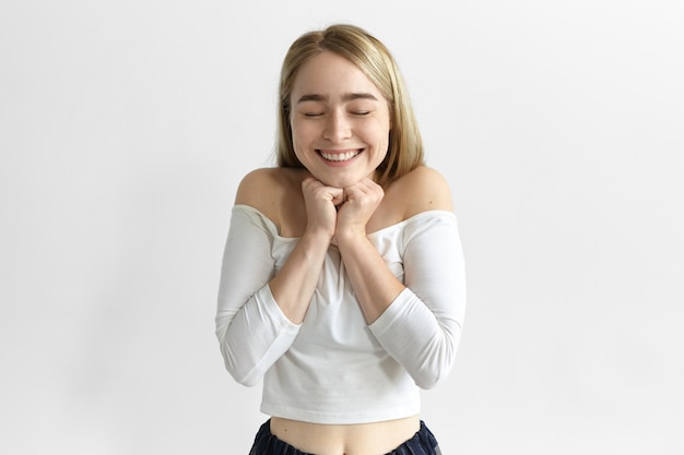 Human facial expressions and body language. emotional ecstatic young blonde woman in stylish clothes closing eyes and smiling excitedly, overjoyed with unexpected gift or news