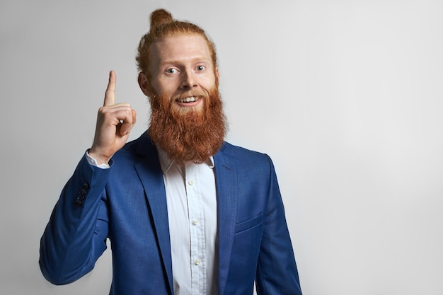 Human facial expressions and body language. Studio shot of attractive fashionable successful young bearded male entrepreneur wearing elegant stylish suit, pointing index finger, having excited look