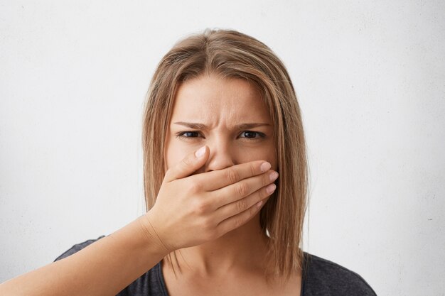 Human facial expressions and emotions. Headshot of scared young woman with bob haircut covering her mouth with hand as if prohibited to say anything, looking with eyes full of terror