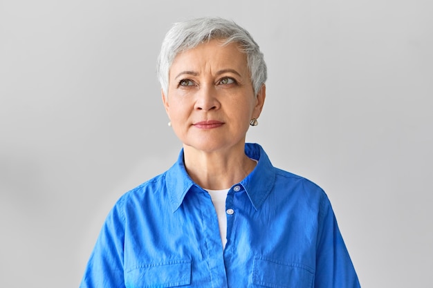 Human facial expressions. Picture of thoughtful fashionable elegant European female designer with pixie haircut looking up with dreamy pensive smile, being inspired with sudden creative idea