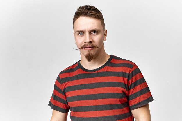 Human facial expressions and reaction. Isolated view of funny stylish young man with waxed mustache and trimmed beard staring at camera in full disbelief, having distrustful surprised look
