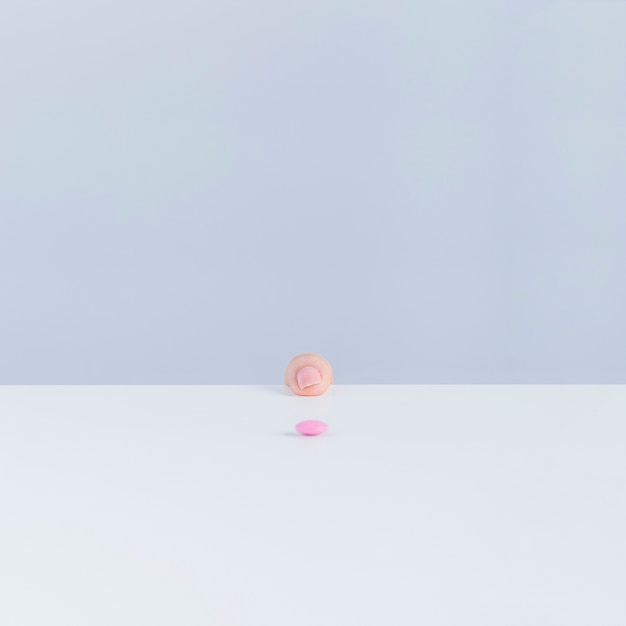 Free photo human finger at the edge of table with pink pill