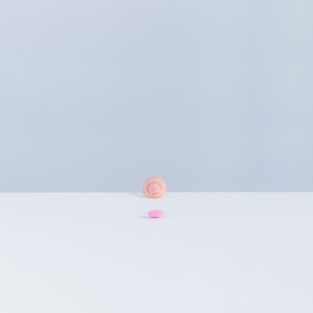 Human finger at the edge of table with pink pill