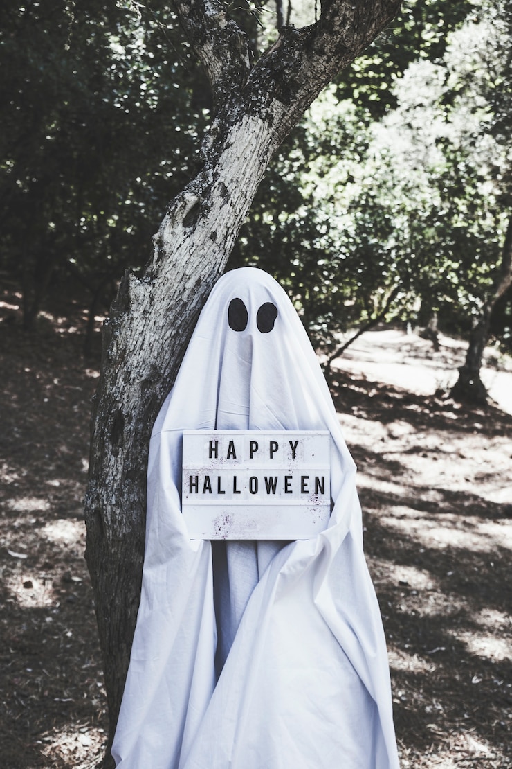 無料Photo ハロウィンのタブレットを持っている森の木の近くの幽霊の衣装の人間