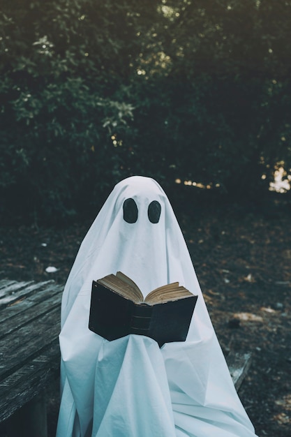 Human in ghost suit sitting on bench and reciting book