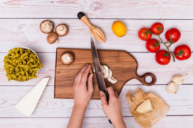 Human hand cutting mushroom for making delicious pasta over wooden surface