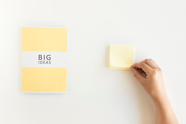 Human hand holding adhesive note besides big ideas diary