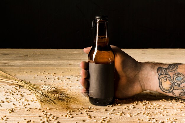 Человеческая рука, держащая алкогольную бутылку с ушами пшеницы на деревянной поверхности