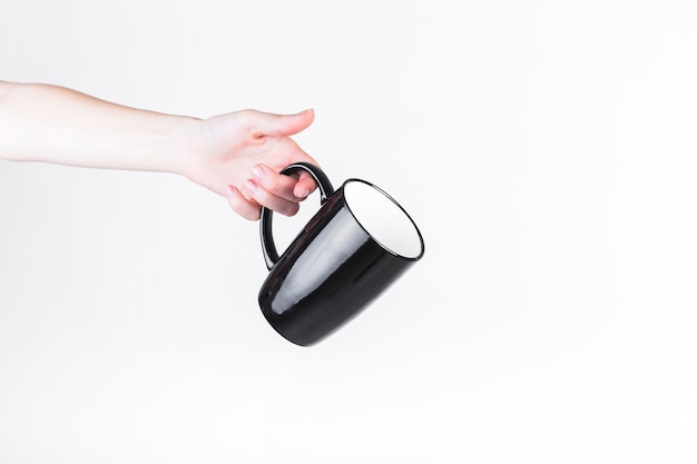 Human hand holding black cup on white backdrop