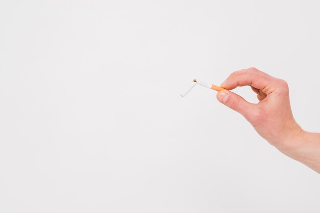 Human hand holding broken cigarette on white backdrop