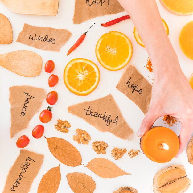 Human hand holding candle near fruits, notes and leaves 