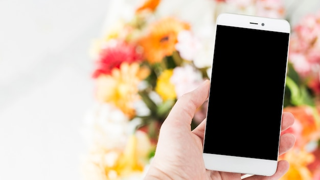 Human hand holding cellphone with flower bouquet in background