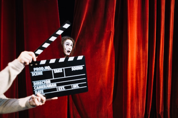 Human hand holding clapperboard in front of male mime artist face