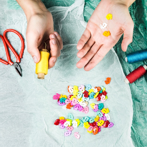 Human hand holding colorful buttons and thread spool with scissor