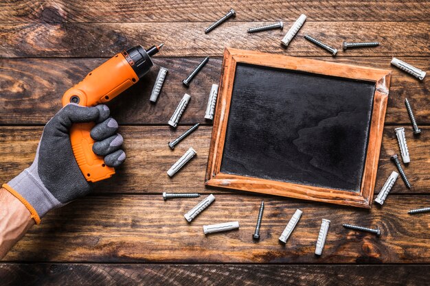 human hand holding cordless drill near screws surrounding blank slate