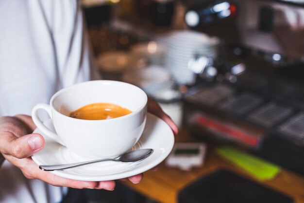 Human hand holding cup of coffee in cafeteria