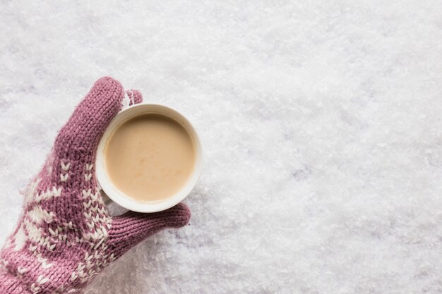 雪に覆われた土地の上に一杯のコーヒーを持っている人間の手