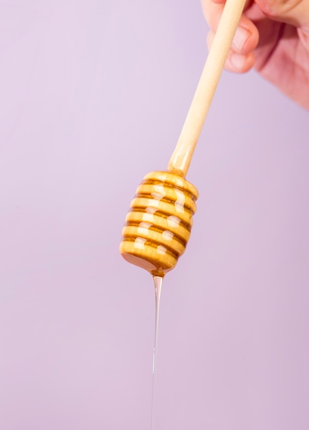 Human hand holding dipper with honey over purple backdrop