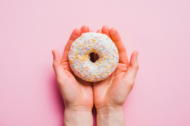 Human hand holding donut on pink background