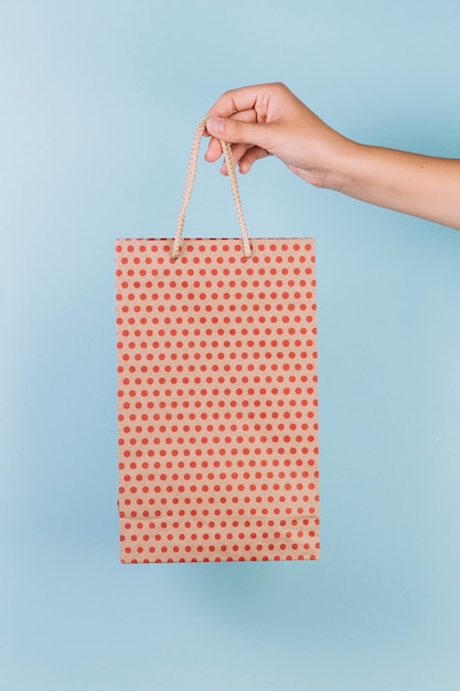 Free photo human hand holding dotted pattern paper shopping bag on blue background