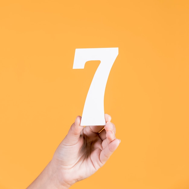 Free photo human hand holding number seven against yellow background