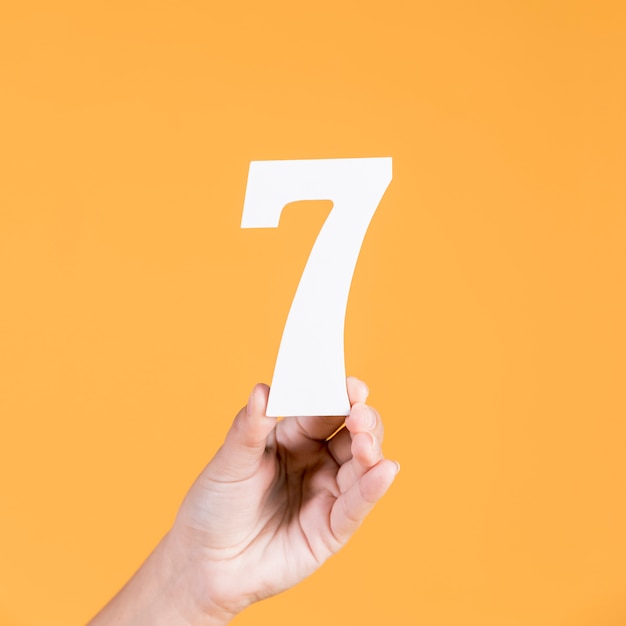 Human hand holding number seven against yellow background