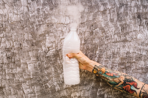 Free photo human hand holding plastic bottle with smoke coming out from it