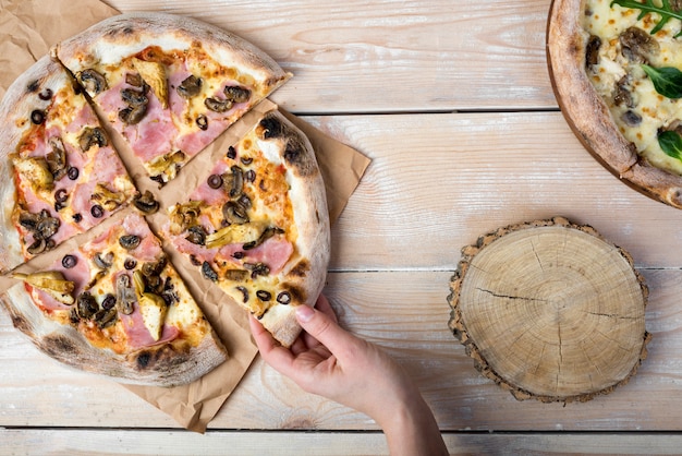 Human hand holding tasty mushroom and bacon pizza on textured wooden plank